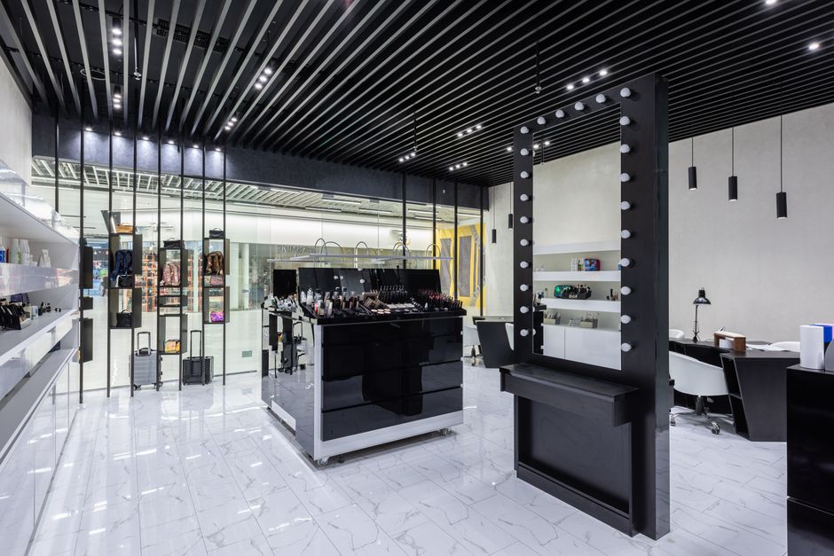 Interior view of a retail store with a modern, minimalistic design, featuring a black and white colour scheme. In the foreground, there is a black dressing room mirror with round bulb lights along its