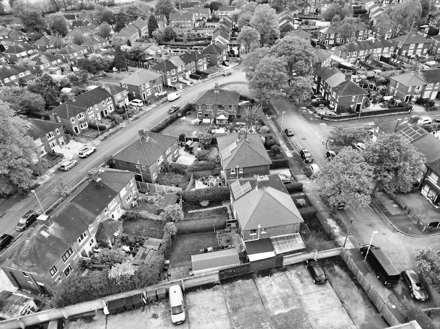 An aerial view taken from a drone showing a residential neighbourhood with a mix of detached and semi-detached houses, many with pitched roofs and small gardens surrounded by fences and hedges. Severa